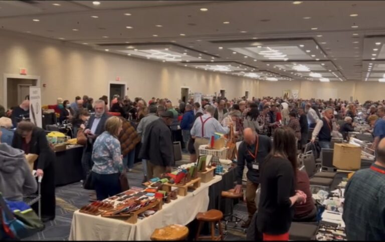 Many people in a conference room looking at display tables at a pen show