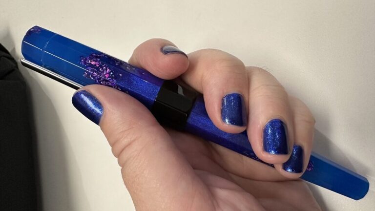 Blue fountain pen being held by fingers with a blue manicure